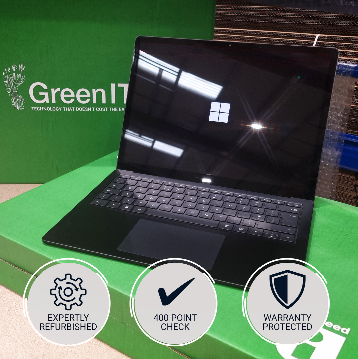 A black refurbished laptop sits open on a green box with the GreenIT logo in the background. Three circular badges at the bottom read 'Expertly Refurbished', '400 Point Check', and 'Warranty Protected'.